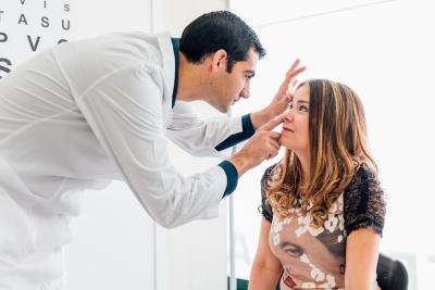 A patient sits while a doctor performs an eye exam.